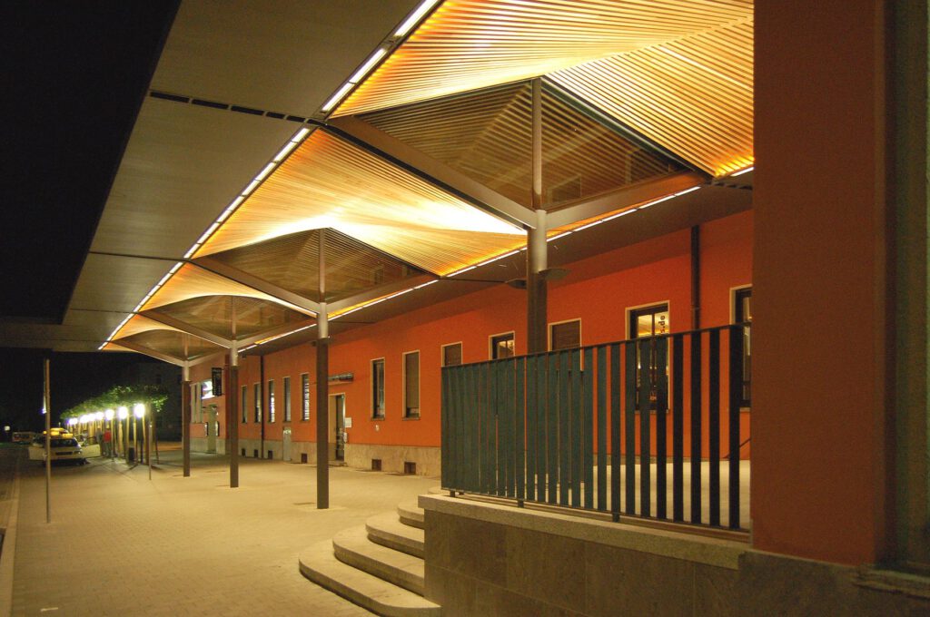 Bussteigüberdachung Ingolstadt bei Nacht – angestrahlte Holzkonstruktion vor der Bahnhofsfassade